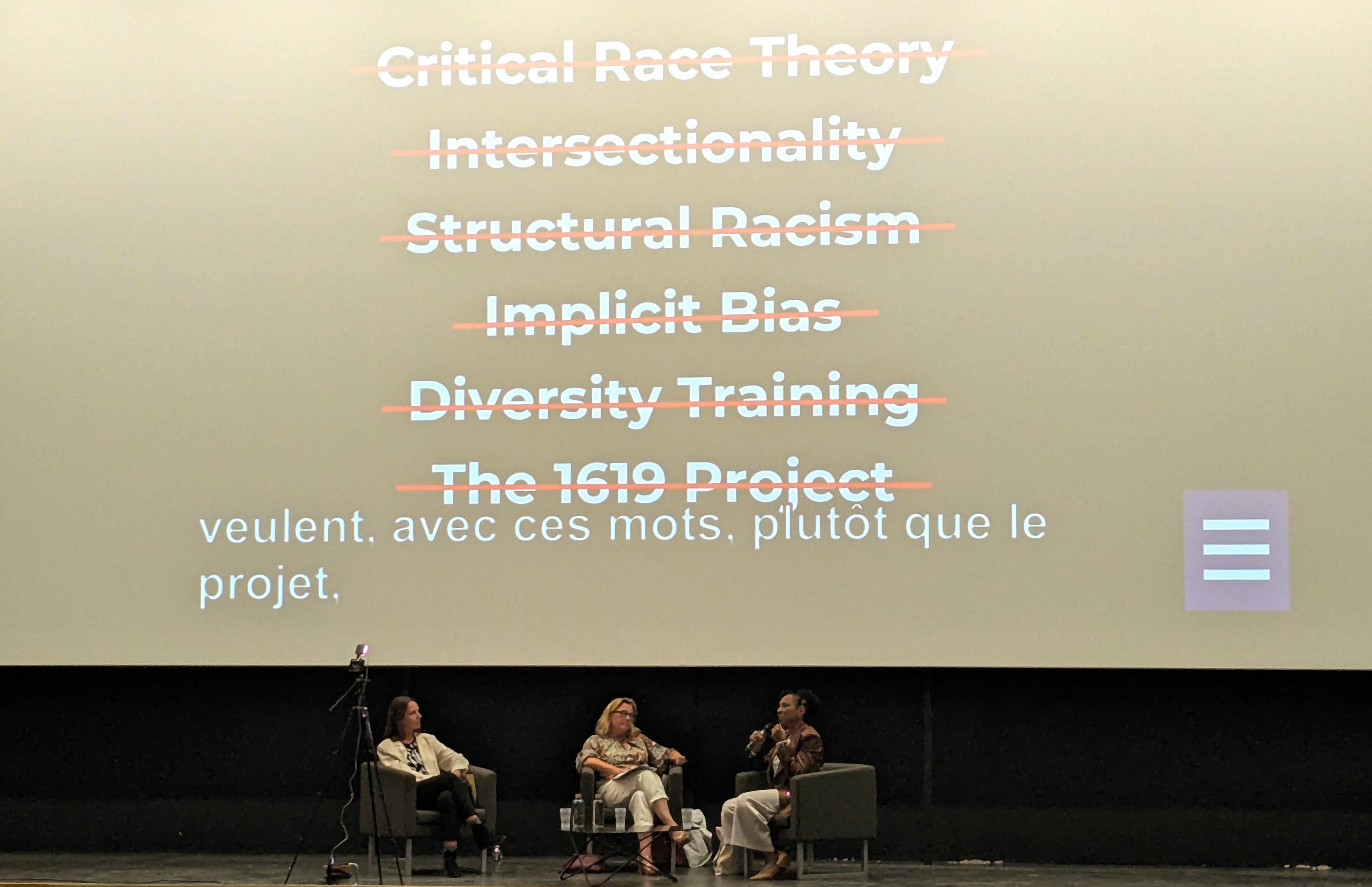 Kimberlé Crenshaw à l'estrade avec Stéphanie Hennette-Vauchez devant une image des mots "critical race theory", "intersectionnality", "structural racims" "implicit bias", "diversity trainig" et "1679 project" barrés en rouge